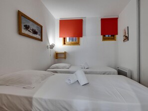 Ein Hotelzimmer mit zwei Betten, einem Bild an der Wand und zwei Fenstern mit roten Jalousien.