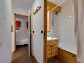 Un dormitorio compacto con una cama individual, un armario de madera con cajones y una zona de ducha con bañera.