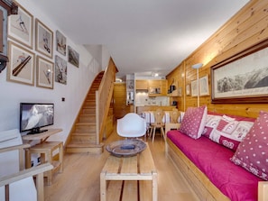Ein gemütliches Wohnzimmer mit einer Holztreppe, einem Fernseher, einem Essbereich und einer Couch mit gemusterten Kissen.