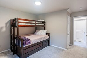 Una cama individual con estructura de madera, cabecera y piecera. Hay dos cajones debajo de la cama y una mesita de noche con una lámpara.