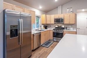A modern kitchen with stainless steel appliances, wooden cabinets, and a white countertop.