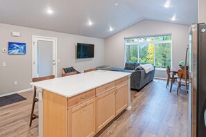 Una cocina moderna con una isla central, un área de comedor con sofá, y un ventanal con vistas al exterior.