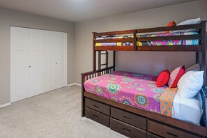 A bunk bed with a colorful bedspread, a white closet with multiple doors, and a carpeted floor.