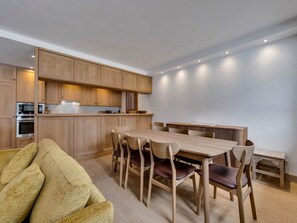A modern kitchen with wooden cabinets, a dining table with chairs, and built-in appliances. - Charming and spacious duplex apartment - 7 guests (Val-d'Isère)