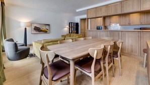Een moderne woonkamer met een houten eettafel, zachte zithoek en een keuken met houten kasten en apparatuur.