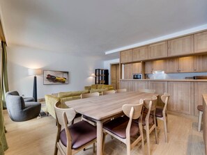 A modern living room with a wooden dining table, comfortable seating, and a kitchen area with wooden cabinets and appliances. - Charming and spacious duplex apartment - 7 guests (Val-d'Isère)