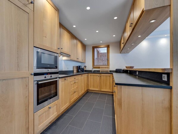 Een moderne keuken met houten kastjes, een ingebouwde magnetron, een oven en een raam met zonwering.
