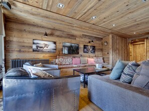 Ein gemütliches Wohnzimmer mit Holzbalkendecke, einer Sofagarnitur, einem Couchtisch und einem Kamin.