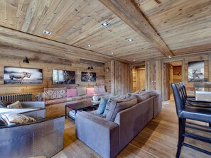 Ein gemütliches Blockhaus-Interieur mit Holzbalkendecke, einer Couch, einem Esstisch und Bildern an den Wänden.