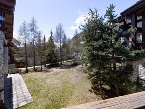 Eine Holzhütte mit Steinwänden, einer Holzterrasse und Blick auf ein bewaldetes Gebiet mit hohen Bäumen.