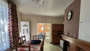 Ein Essbereich mit einem für vier Personen gedeckten Tisch, Holzstühlen, einer Chandelierleuchte, einer Küche mit Backsteinwand und einer Wanduhr.