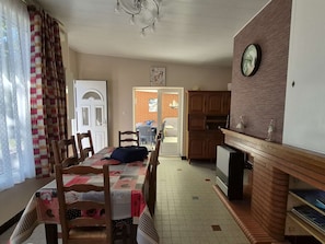 Ein Essbereich mit einem für vier Personen gedeckten Tisch, Holzstühlen, einer Chandelierleuchte, einer Küche mit Backsteinwand und einer Wanduhr.