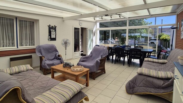 Ein Wintergarten mit Glastür zum Garten, eingerichtet mit Sofas, einem Tisch und Stühlen.
