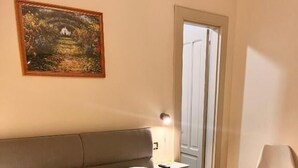 Et hotelværelse med seng, puder, sammenfoldede håndklæder, et natbord med lampe, en stol og en dør.