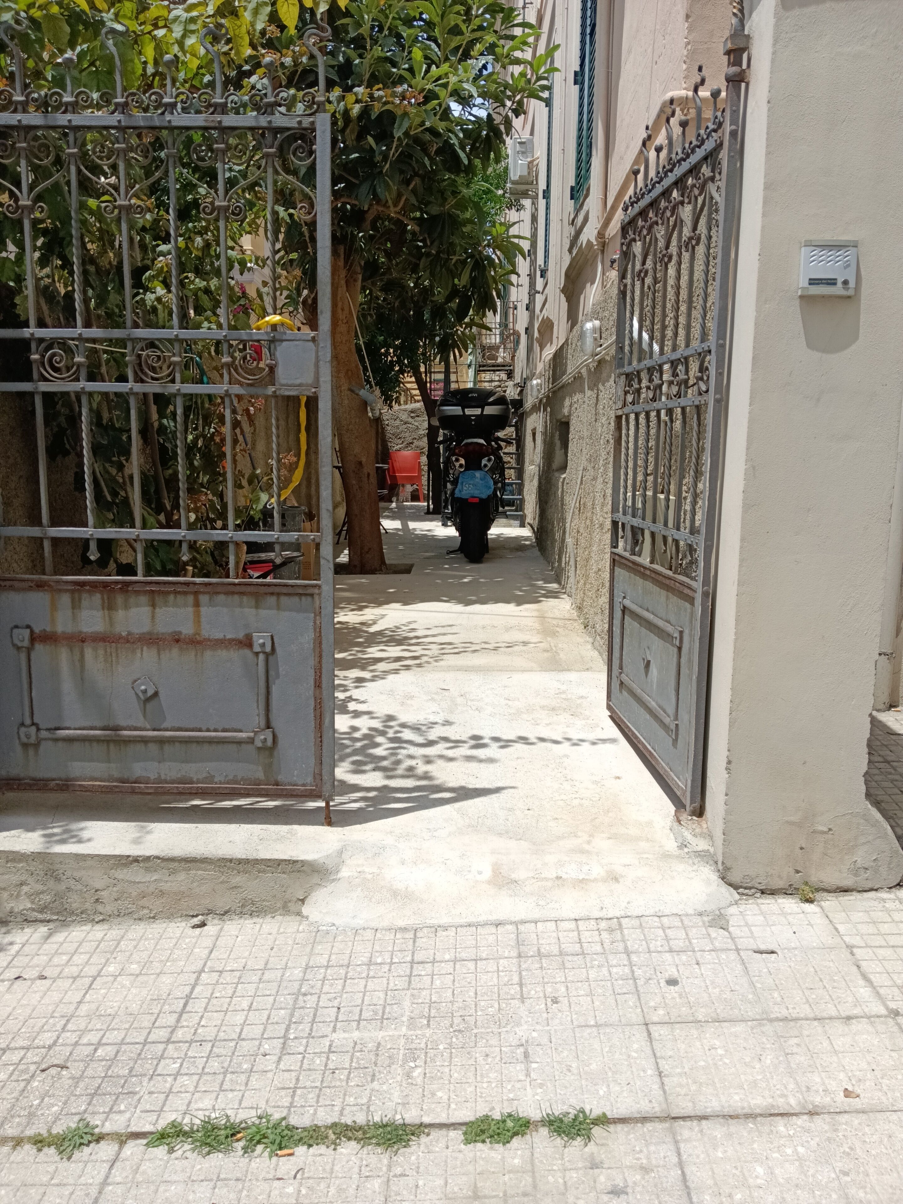 A narrow alleyway with a metal gate, a tree, and a parked motorcycle.