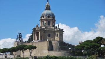 Um edifício histórico com cúpula e estátuas, rodeado por árvores e um céu claro.