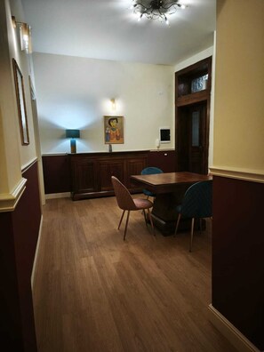A dining area with a wooden table and chairs, a wall-mounted lamp, and a painting.