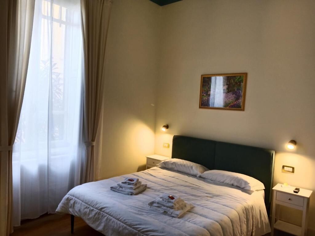 Une chambre à coucher comprenant un lit, deux tables de chevet, une commode, une fenêtre avec des rideaux et un tableau encadré accroché au mur.