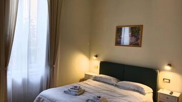 Une chambre à coucher comprenant un lit, deux tables de chevet, une commode, une fenêtre avec des rideaux et un tableau encadré accroché au mur.