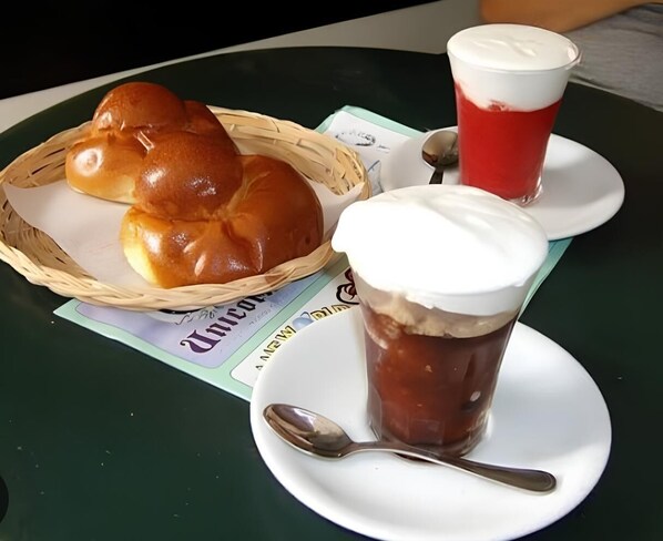 A table with a basket of bread, a cup of iced coffee, and a spoon.