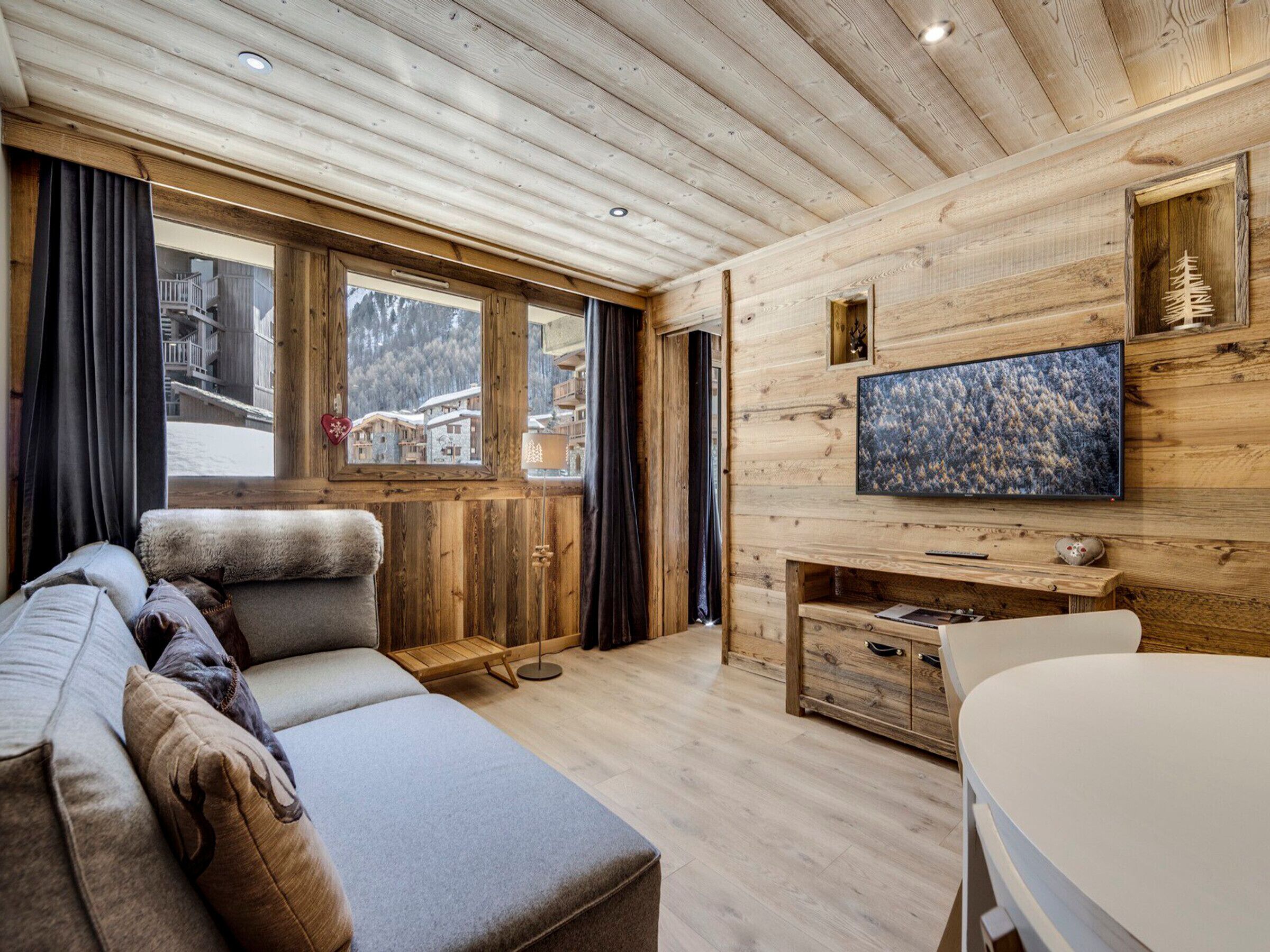 Ein gemütliches Zimmer mit Holzvertäfelung, einer Couch, einem Fernseher und Blick auf einen verschneiten Berg.