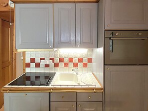 A kitchen with grey cabinets, a black stove, a white sink, and a red and white tiled backsplash. - Charming apartment - 4 guests, forest view (Méribel)