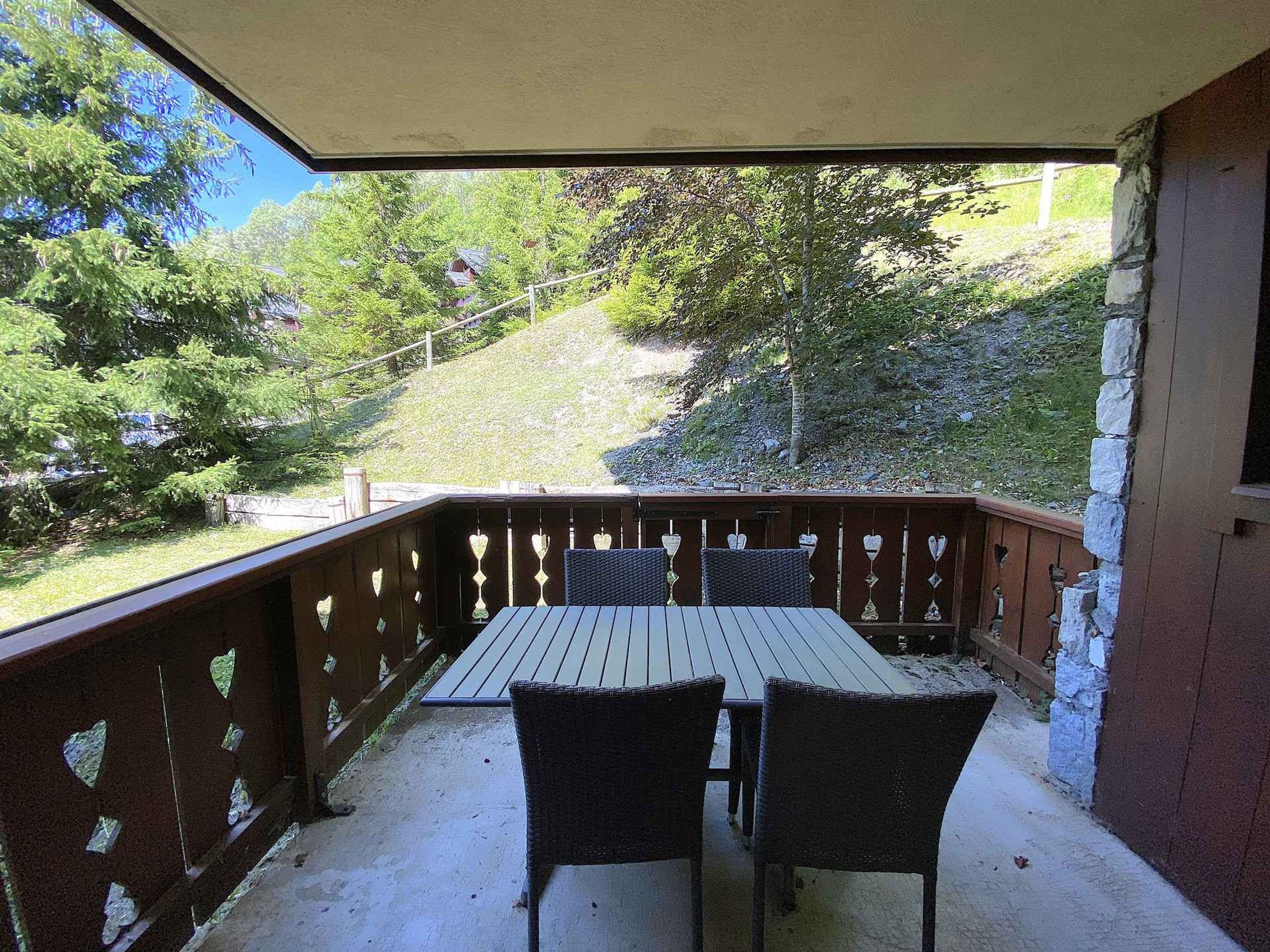 A covered patio with a wooden table and chairs, surrounded by a wooden railing with heart-shaped cutouts.