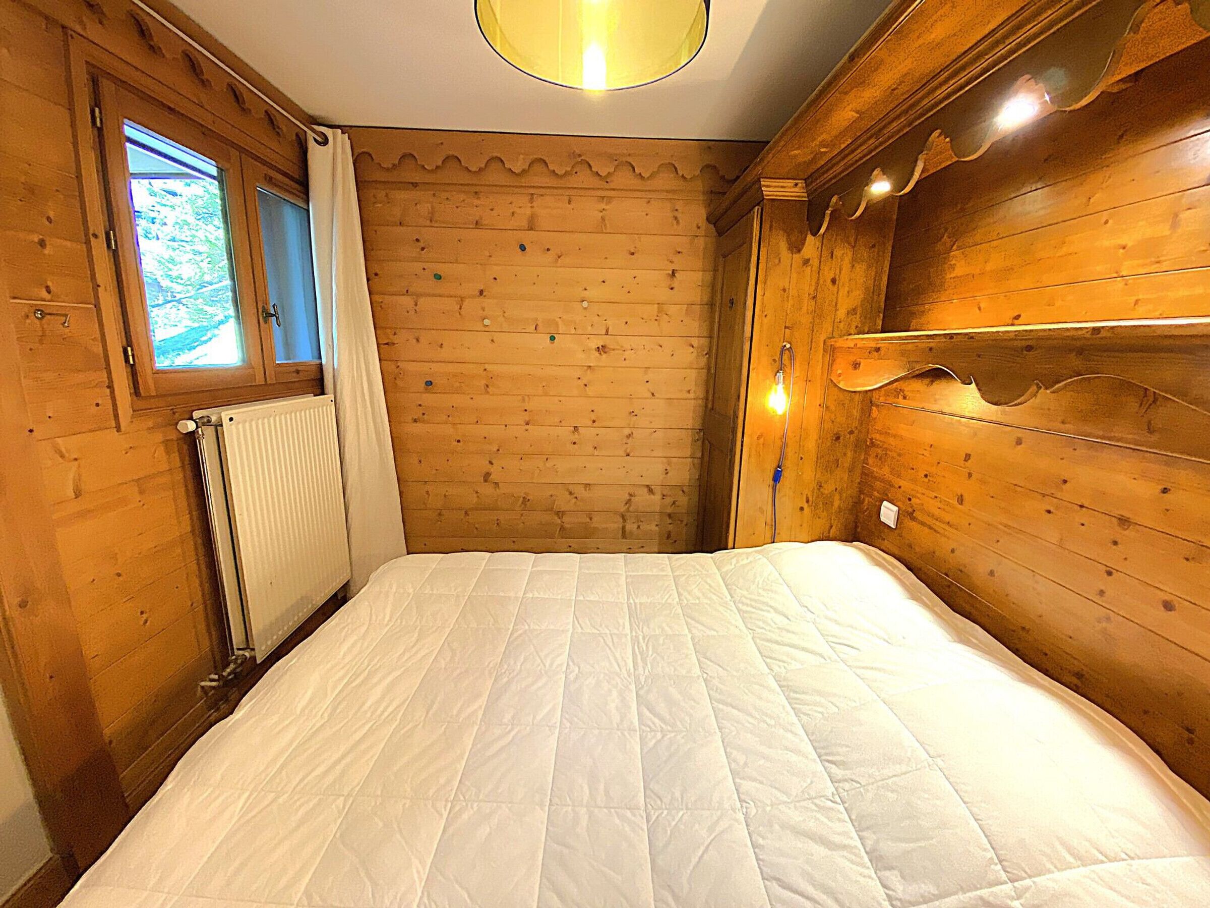 Ein Zimmer mit Holzboden, einem Bett, einem Fenster und einer Heizung.