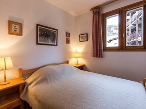 Quarto com cama, duas mesas de cabeceira, janela com cortinas e quadros nas paredes.