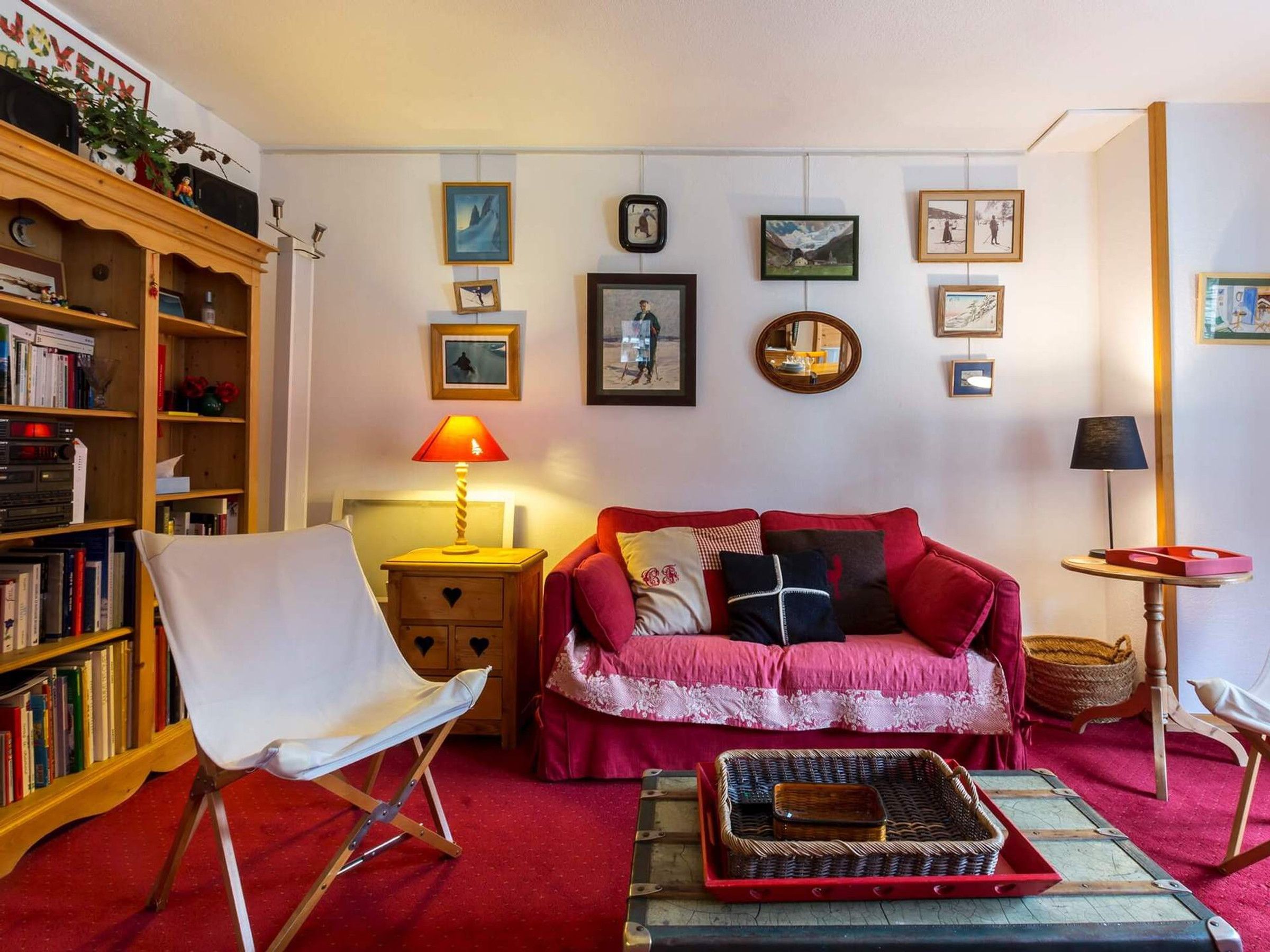 A cozy living room with a red sofa, a white armchair, and a bookshelf filled with books.