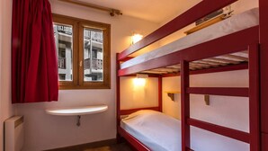 Quarto pequeno e funcional com beliche, janela com cortinas, mesa de cabeceira e radiador.