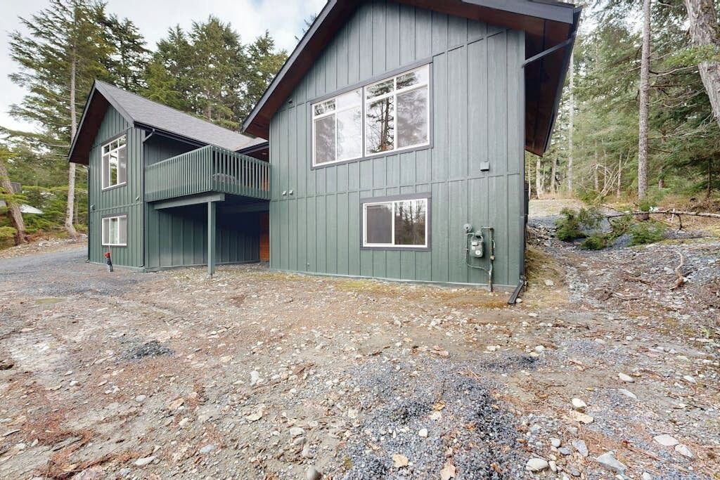 A two-story cabin with a balcony, surrounded by a forested area.