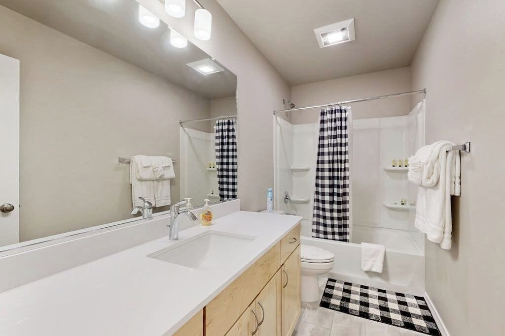 A modern bathroom with a large mirror, a double sink, a toilet, and a shower area.