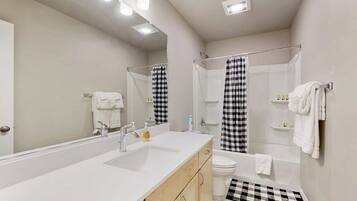 A modern bathroom with a large mirror, a double sink, a toilet, and a shower area.