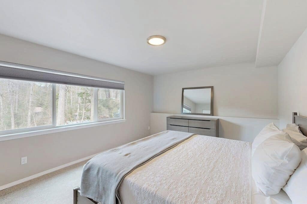 A bedroom with a bed, a dresser, a mirror, and a window.