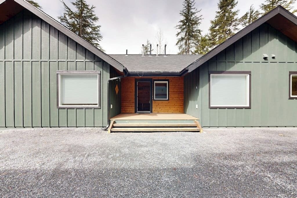 A two-story building with a wooden front door, a small porch, and a gravel driveway.