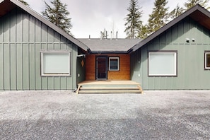 A two-story building with a wooden front door, a small porch, and a gravel driveway.