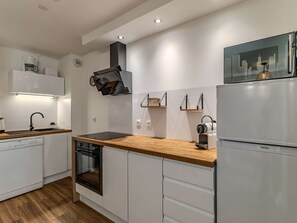 Una cocina moderna con armarios blancos, horno empotrado, campana extractora negra y refrigerador de acero inoxidable.