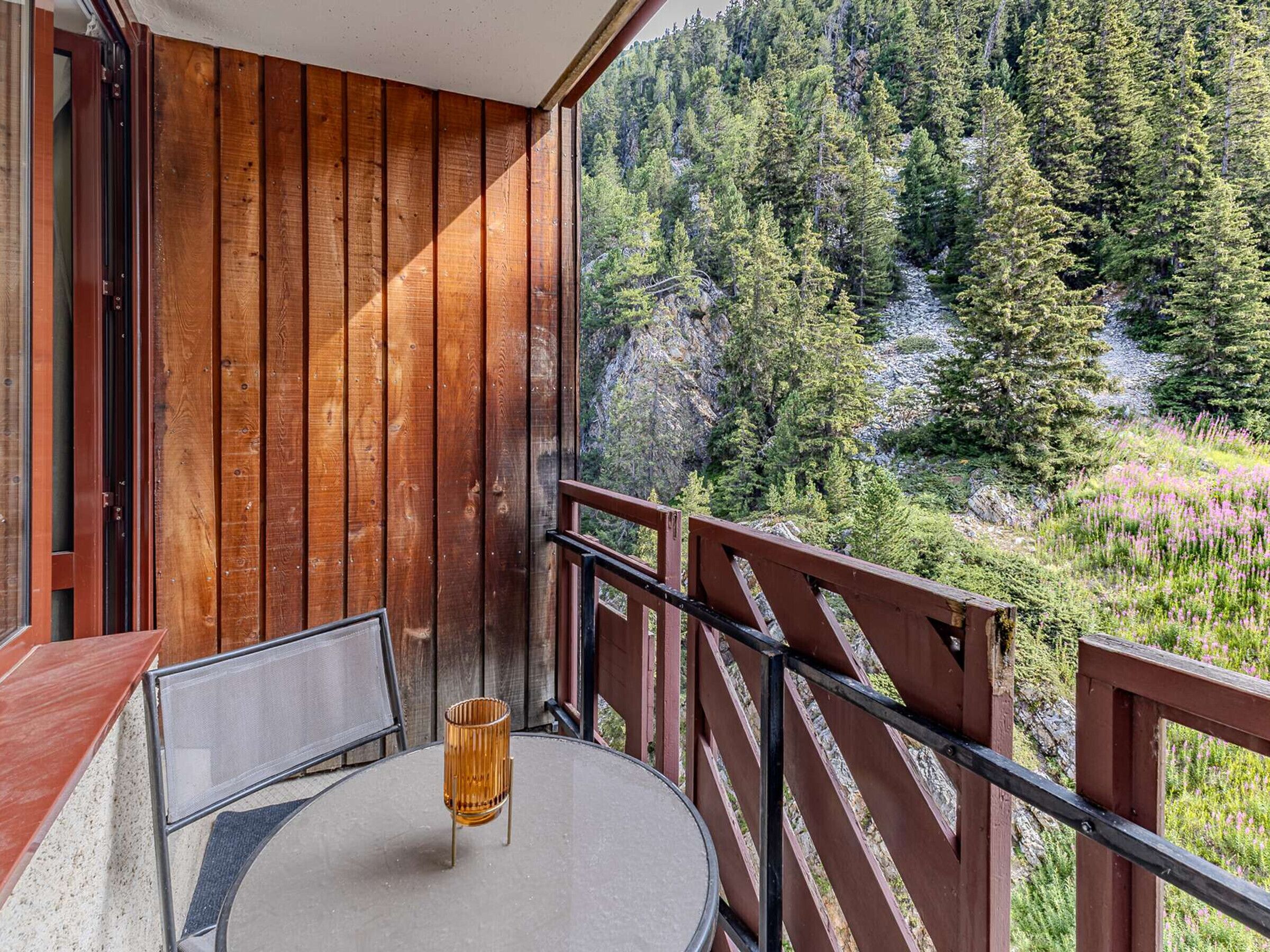 A balcony with a table and chairs, overlooking a forested area.