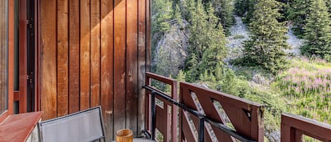 A balcony with a table and chairs, overlooking a forested area.