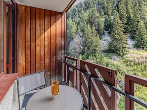 A balcony with a table and chairs, overlooking a forested area. - Cozy apartment near slopes - 4 guests (Plagne Bellecôte)