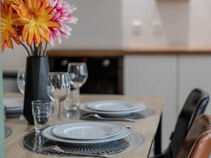 Una mesa de comedor dispuesta con platos, vasos y cubiertos, con un florero en el fondo.