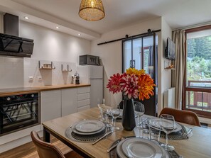 A modern kitchen with white cabinetry, a built-in oven, and a dining area set for six with a wooden table and six chairs. - Cozy apartment near slopes - 4 guests (Plagne Bellecôte)