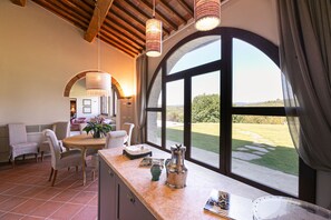 A dining area with a large window, a table with chairs, and a kitchen counter with various items. - Casa Faraona Villa With Private Pool (Gaiole in Chianti)
