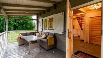 A covered outdoor seating area with a sofa and table, wooden walls, and a staircase leading to an interior room.