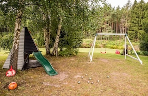 A playground with a slide and swing set, surrounded by trees and a grassy area.