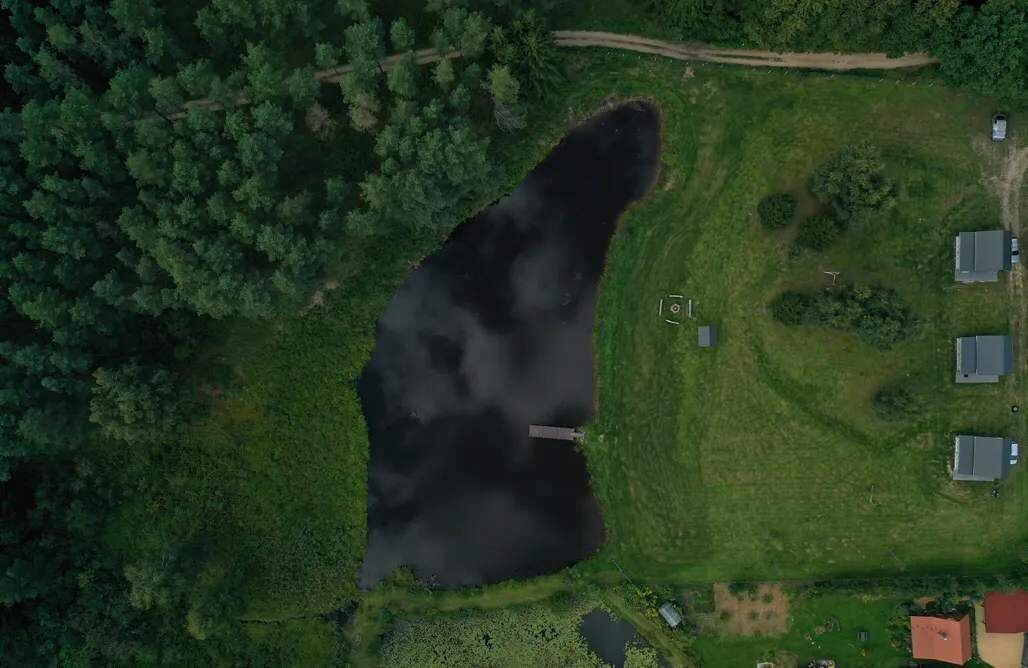 Eine Luftaufnahme eines Anwesens mit einem großen Teich, umgeben von üppiger Vegetation und einigen Gebäuden.