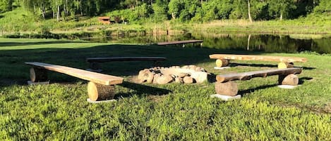 A picnic area with benches and a fire pit surrounded by grass and trees.