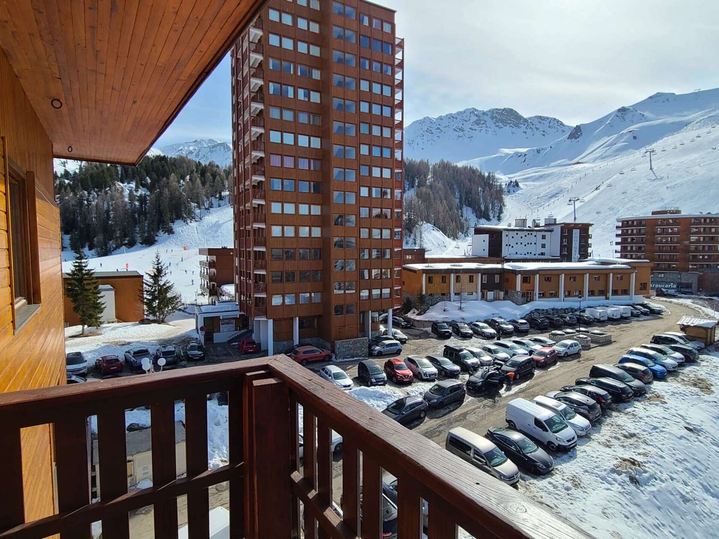 A high-rise building with multiple floors, a parking lot with several cars, and a snowy mountainous landscape in the background.