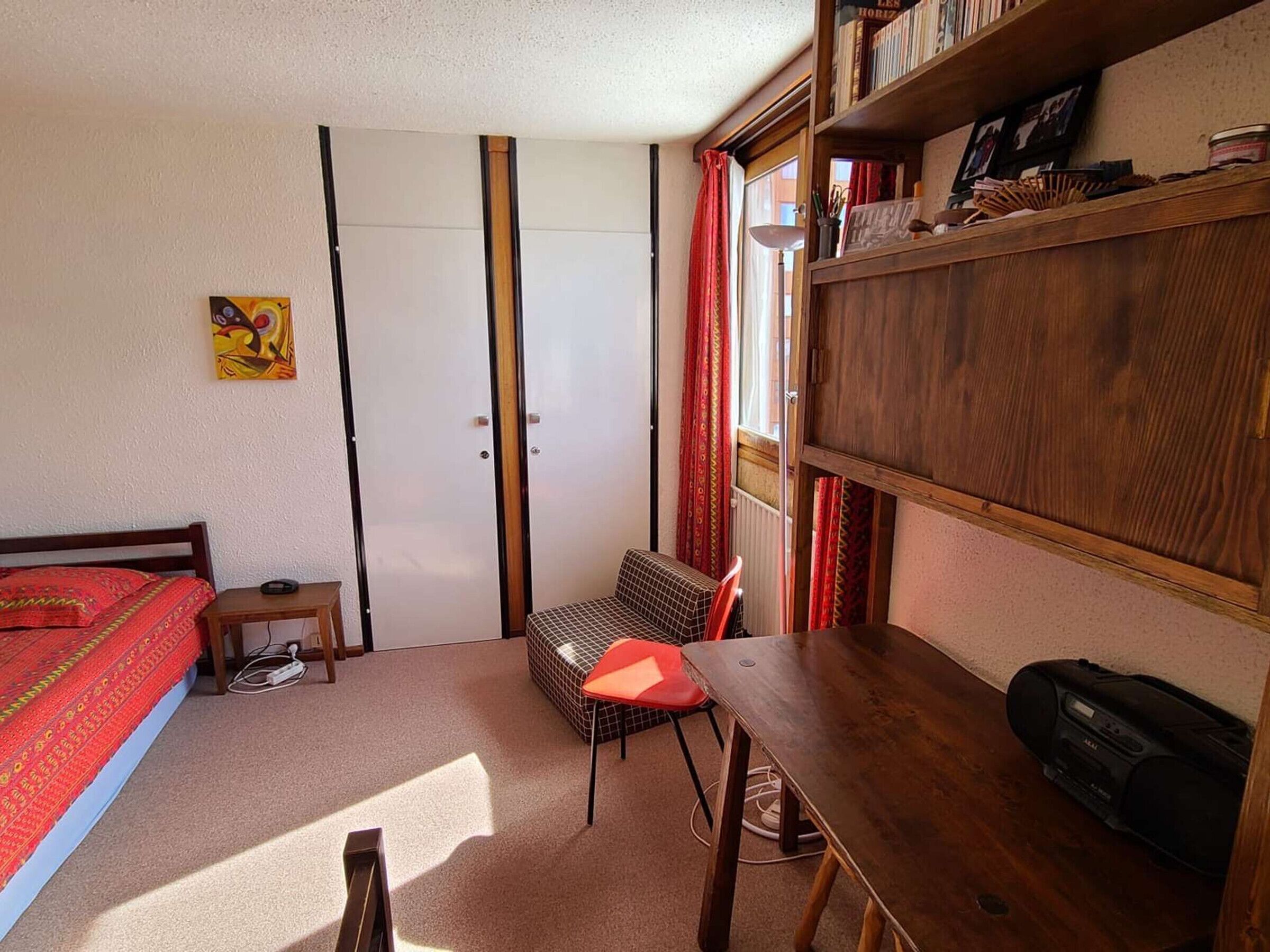 Une chambre à coucher comprenant un lit, un bureau, une chaise, une bibliothèque et un radiateur.